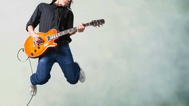 Male Guitarist playing music on grey wall background © BillionPhotos.com
