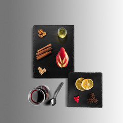 Mulled wine recipe ingredients and kitchen accessories, bottle of red wine, cinnamon, anise stars, orange, brown sugarand spice on gray background.
