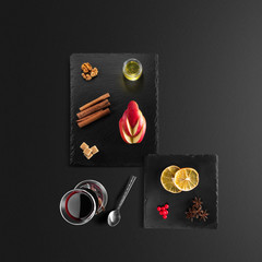 Mulled wine recipe ingredients and kitchen accessories, bottle of red wine, cinnamon, anise stars, orange, brown sugarand spice on black background.