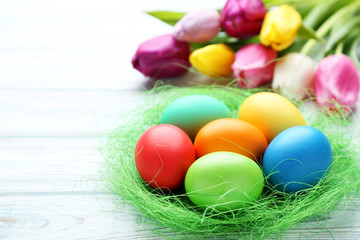 Colorful easter eggs in nest with tulips on wooden table