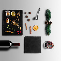 Mulled wine recipe ingredients and kitchen accessories, bottle of red wine, cinnamon, anise stars, orange, brown sugarand spice on gray background.