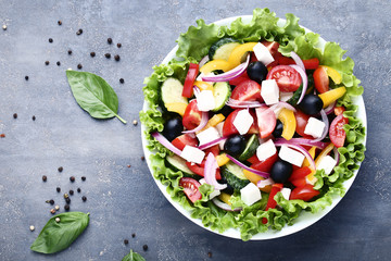 Vegetable salad in bowl with basil leafs on grey background