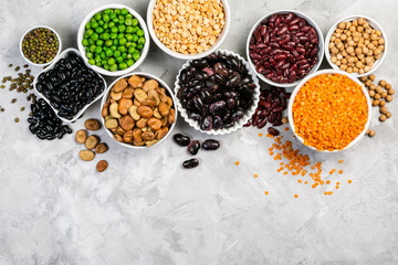 Selection of legumes - beans, lentils, mung, chickpea, pea in white bowls on stone background