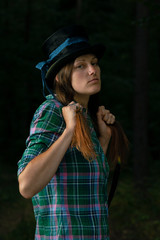 The young woman wears a green shirt and hat posing in a dark forest. Serious portrait of a woman looks like a witch.