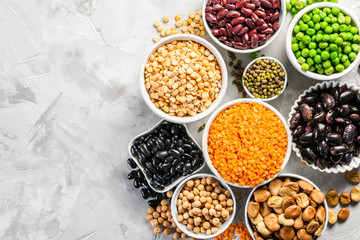 Selection of legumes - beans, lentils, mung, chickpea, pea in white bowls on stone background