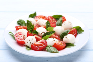 Mozzarella, tomatoes and basil leafs in plate on wooden table