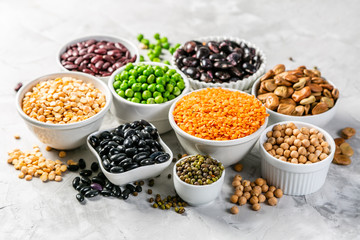 Selection of legumes - beans, lentils, mung, chickpea, pea in white bowls on stone background - obrazy, fototapety, plakaty