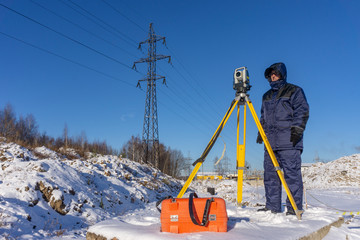 Surveyor in winter in overalls conducts a topographical survey for the cadastre