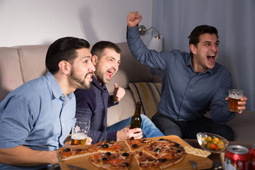 Happy men emotionally watching tv with beer and pizza at home