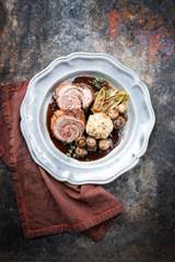Traditional rolled boar roast with bread dumpling, fried chicory and mushroom as top view on a pewter plate in game red wine sauce