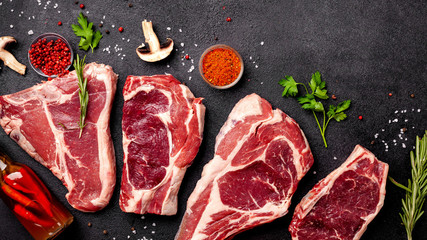 Meat raw steaks lie on a black background with vegetables, tomatoes, marasmade, mushrooms. background image. side view, copy space, top view