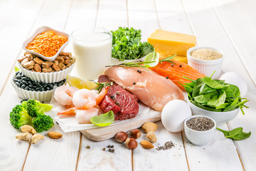 Selection of animal and plant protein sources - fish, meat, beans, cheese, eggs, nuts and seeds, kale, on wood background