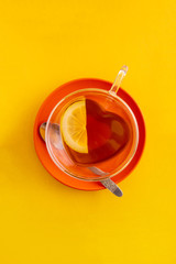 Cup black tea heart shaped cup and red saucer, top view on yellow background