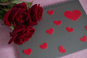 three red roses lie on a grey blank card with red heard, roses and a grey card on a pink background and gray card (close up)