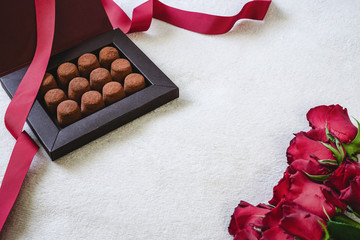 Box of chocolate truffles with red ribbon and red roses. Valentine's Day or romantic celebration concept with copy space