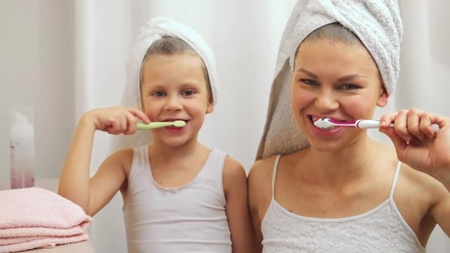 Joyful child with her mother brushing teeth after bath. Concept of dental care and hygiene.