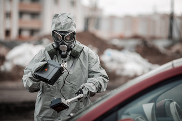 radiation supervisor in protective clothing and gas mask with geiger counter checks the level of...