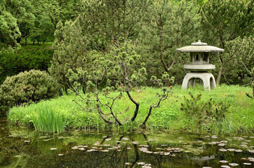 Stone lantern, coniferous trees, pond in traditional Japanese garden.
