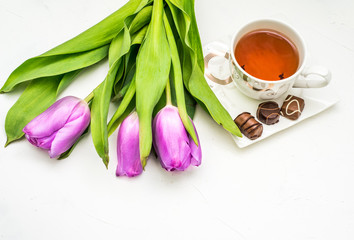 Bouquet of tulips and cup of tea on white background. Holiday card. Soft focus, copy space. Spring concept.