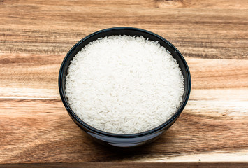 Raw rice in a  black bowl on wooden background 