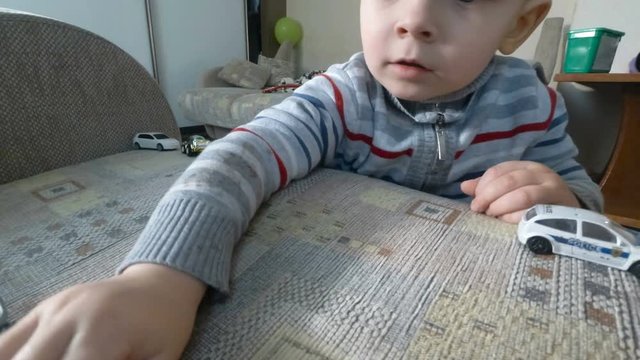 A little baby boy playing with his toys on armchair. Toddler boy is playing with toy cars.