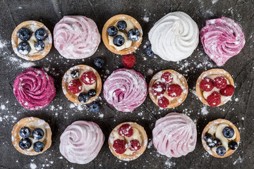Blueberry and raspberry tartlets and marshmallow with cream on dark  background. Top view.