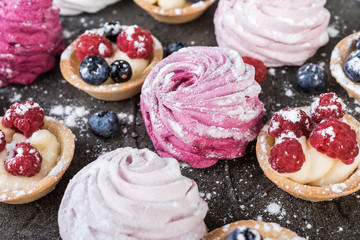 Fototapeta na wymiar Blueberry and raspberry tartlets and marshmallow with cream on dark background.
