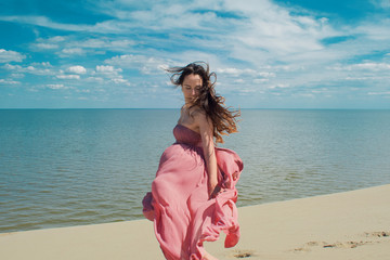 Woman in red waving dress with flying fabric runs on background of dunes.