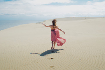Woman in red waving dress with flying fabric runs far away, back view.