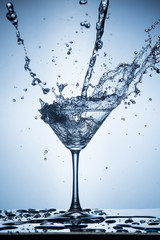 Splashing water on blue background. Cocktail glass with water.