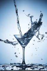Splashing water on blue background. Cocktail glass with water.