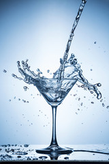 Splashing water on blue background. Cocktail glass with water.