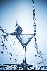 Splashing water on blue background. Cocktail glass with water.