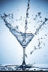 Splashing water on blue background. Cocktail glass with water.