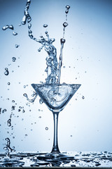 Splashing water on blue background. Cocktail glass with water.