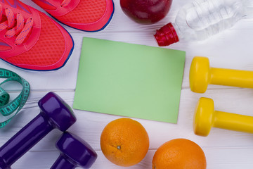 Healthy lifestyle concept. Fitness frame with sneakers, dumbbells, measuring tape, water bottle, fresh fruits and blank paper card.