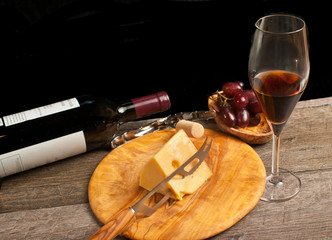 Top view, medium distance of a rare wood plate of french cheese with a cheese knife , bottle of red wine wood bowl of grapes and a stem glass of wine at a french wine tasting event