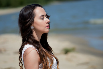 Young beautiful brunette woman in white dress on the seashore.