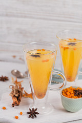 Two high glasses with colorful hot sea buckthorn tea with cinnamon sticks, anise stars and fresh sea buckthorn berries