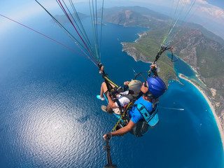 Obraz na płótnie Canvas Paragliding in the sky. Paraglider tandem flying over the sea with blue water and mountains in bright sunny day. Aerial view of paraglider and Blue Lagoon in Oludeniz, Turkey. Extreme sport. Landscape