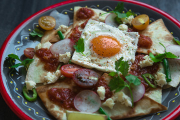 Chilaquiles Mexican tortilla with tomato salsa, chicken and egg close-up on a plate. Horizontal view from above
