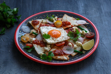 Chilaquiles Mexican tortilla with tomato salsa, chicken and egg close-up on a plate. Horizontal view from above