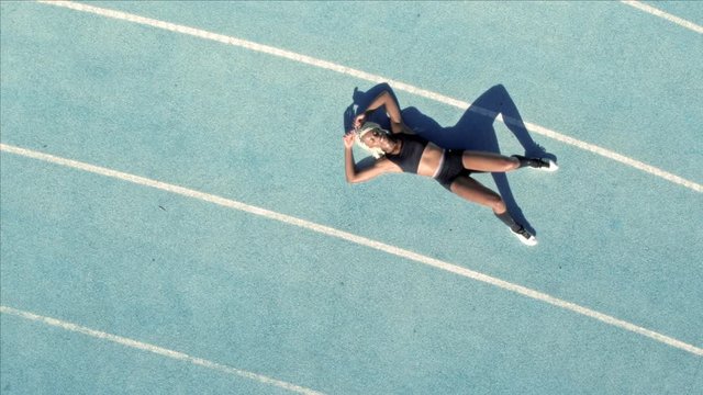 Tired female sprinter resting on athletic track. Top view of exhausted female runner lying on race track after a practice run.