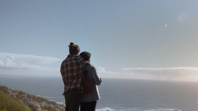 Man embracing his girlfriend from behind and looking at the sea. Couple in love admiring the seascape view.
