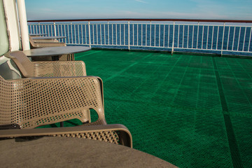 food terrace in a boat with brown plastic chairs and tables, a green plastic floor, railing and the view from the ship to the atlantic ocean 