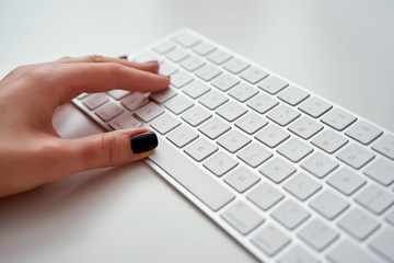 Closeup of female hands typing on white keyboard who is working at office and using computer