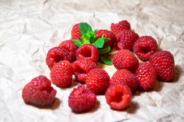A small pile of juicy delicious red raspberries decorated with fresh mint on the plain bright paper background