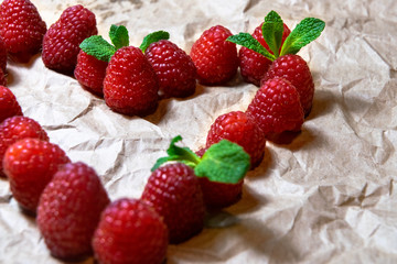 A heart shaped juicy delicious red raspberries decorated with fresh mint on the plain bright background