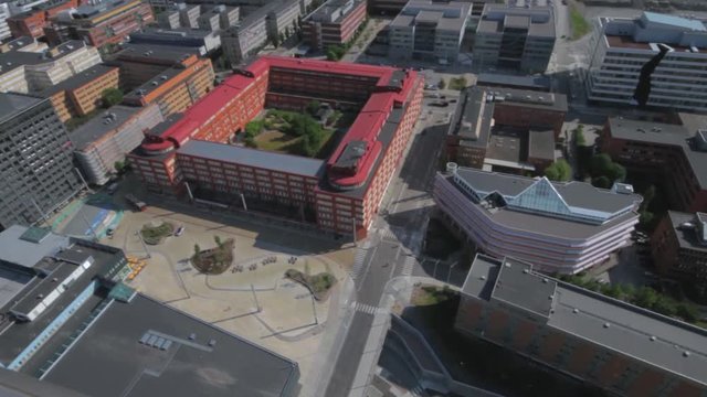 High altitude wide view of the KTH Royal Institute of Technology campus in Kista. Bright red buildings form a square with a courtyard in the middle. Modern architecture of campus buildings.