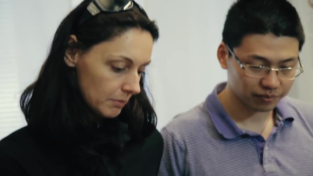 Close up of woman speaking with a young Chinese student. TILT DOWN to a yellow control box in her hands as she explains how to operate the equipment. Professor giving directions to a student.